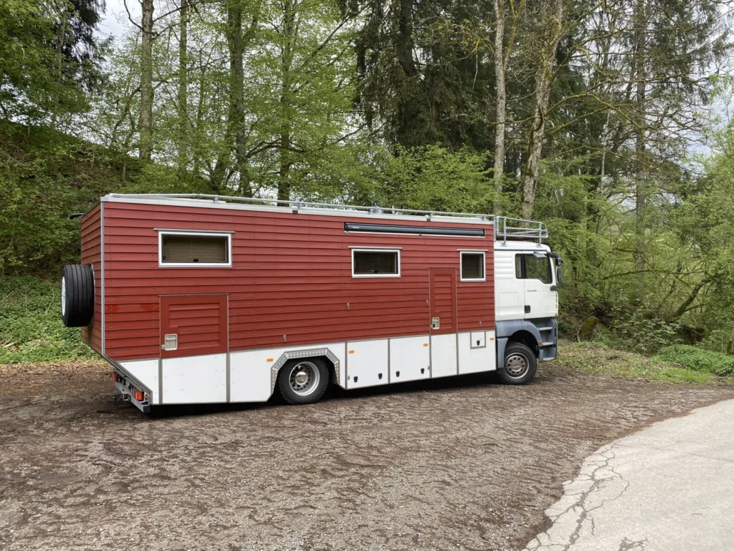 Der MAN mit roter Holzverschalung und Dachreling im Wald geparkt