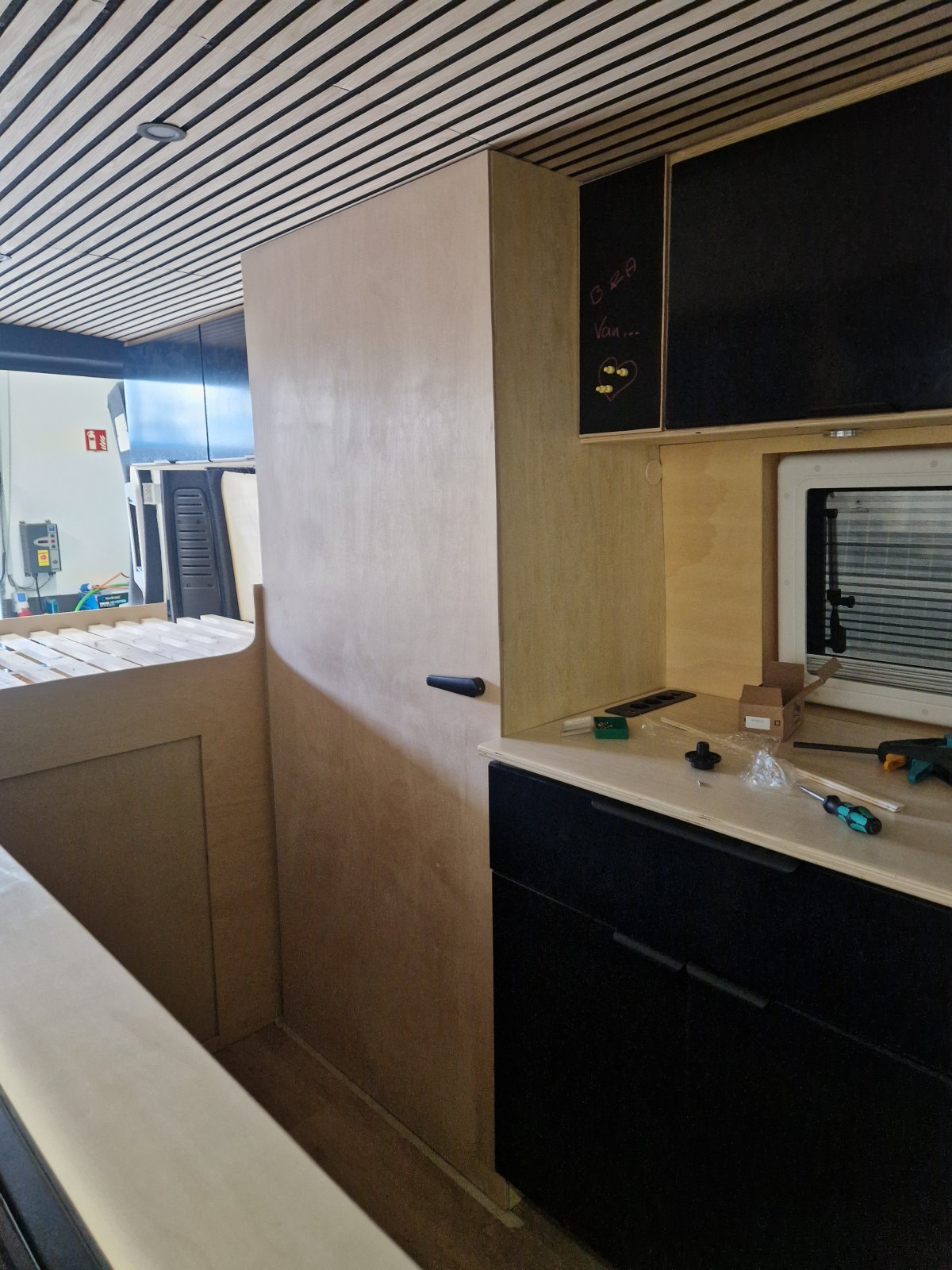 Küchenblock mit schwarzen Fronten, Bett und Paneeldecke